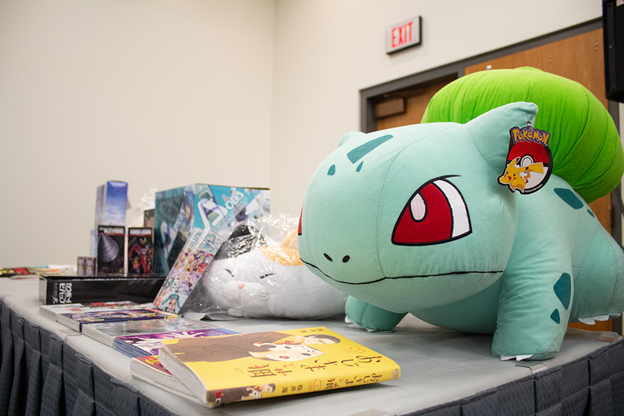 2026 24 A giant Bulbasaur plush among other books and model kits on a table.