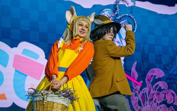 Two cosplayers in matching blue and gold outfits posing on stage with their arms raised