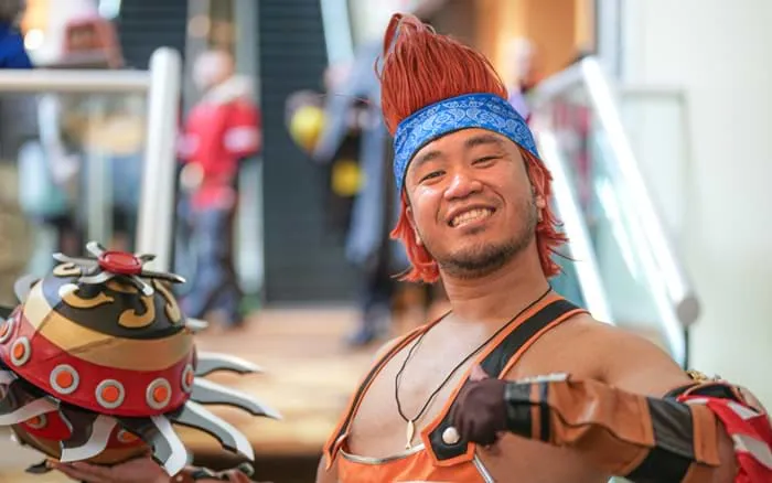 A cosplayer with spiky blond hair and a red scarf carrying a giant sword over one shoulder